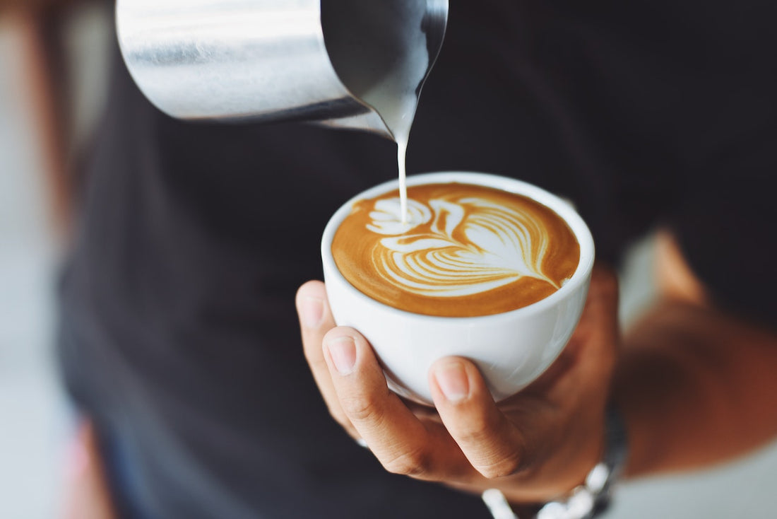 hand pouring steamed milk into espresso to make latte art in the shape of a flower