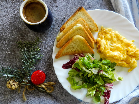 a breakfast plate with egg, salad, and toast accompanied by a cup of coffee