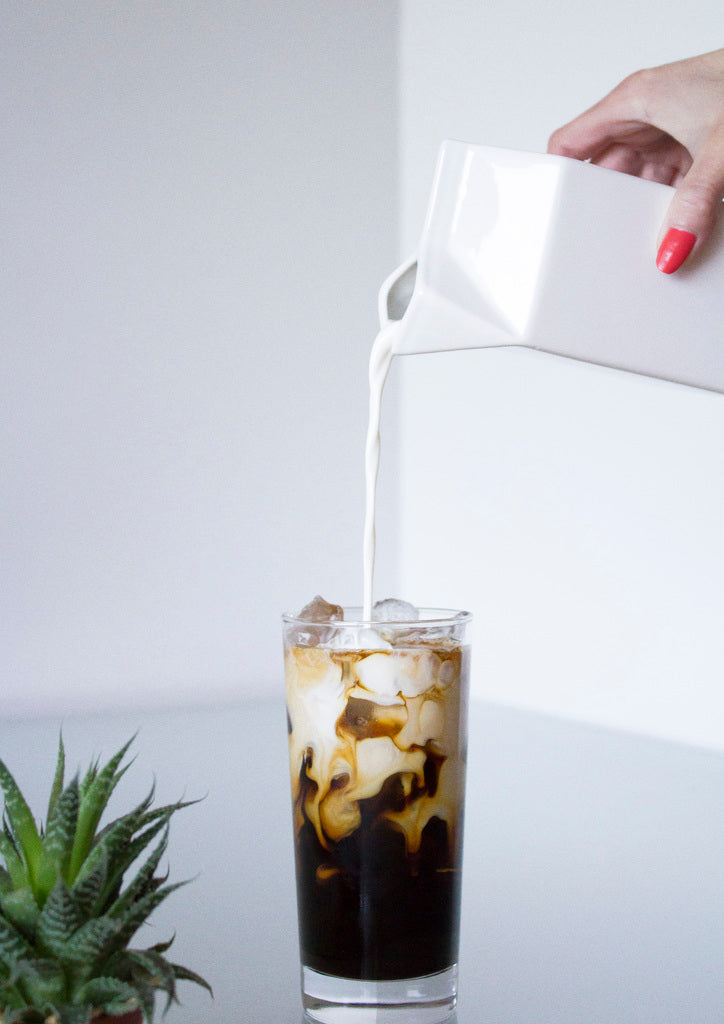Woman's hand pouring milk from a carton into a glass of iced coffee